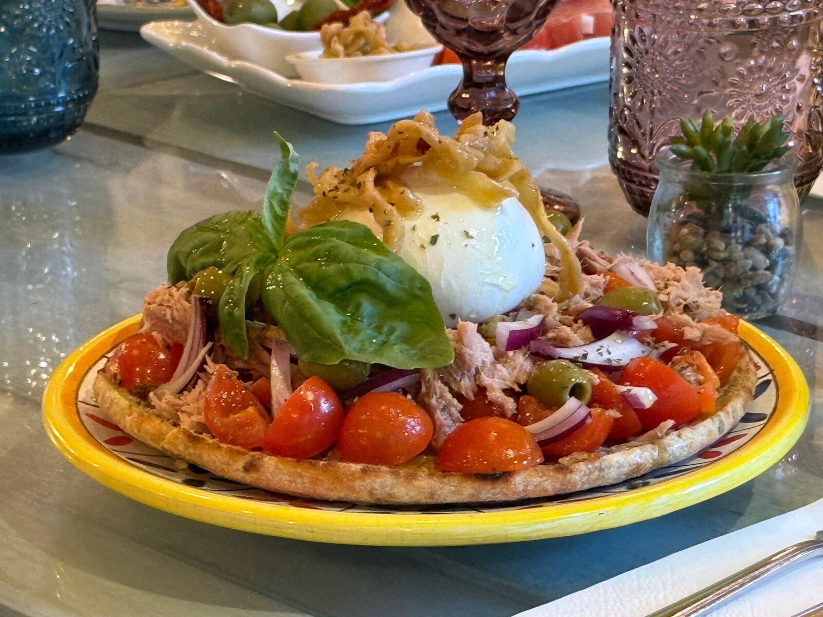 Pane cunzato topped with tuna, burrata, onion and basil on a majolica plate